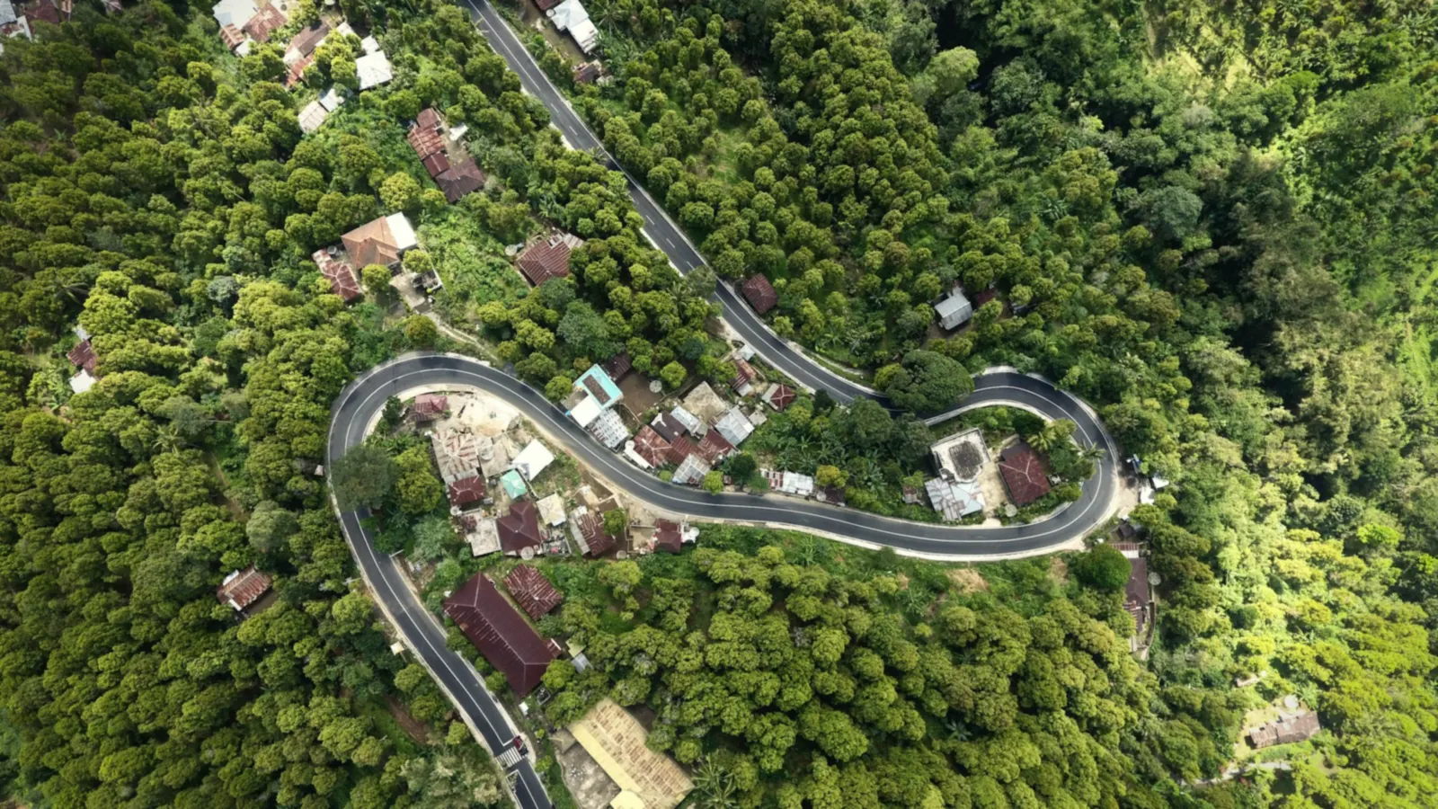 Aerial view of a winding hairpin road through forest and a village near Gitgit, North Bali