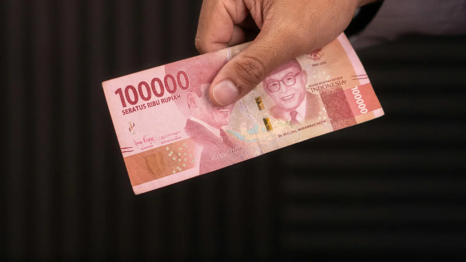 Hand offering an Indonesian 100,000 rupiah banknote as a tip