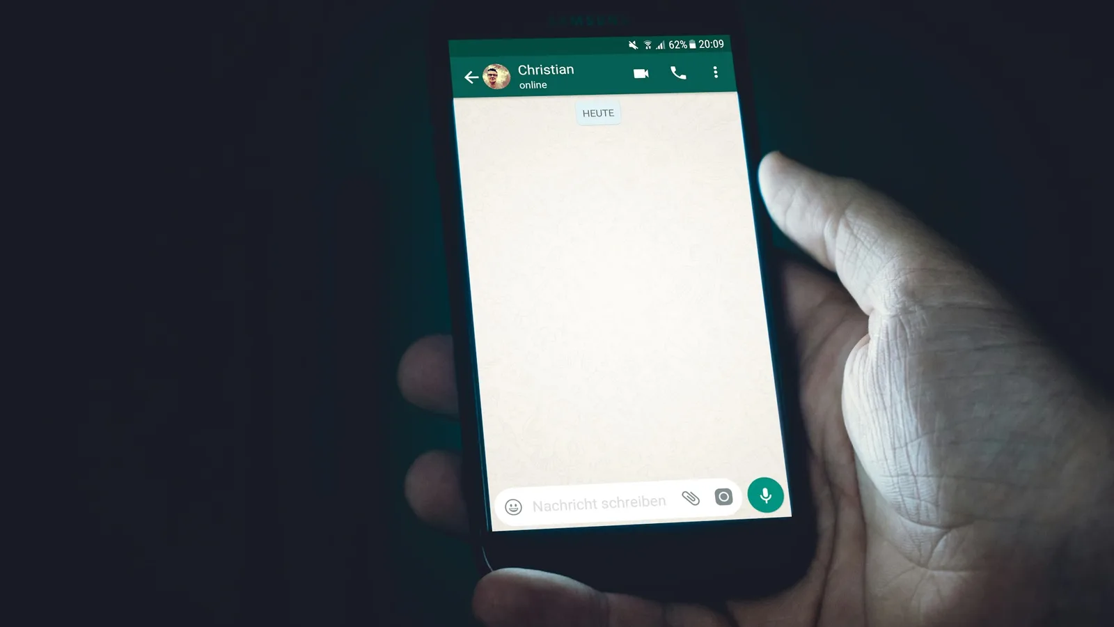 Hand holding a smartphone with an open WhatsApp chat window, ready to message a driver
