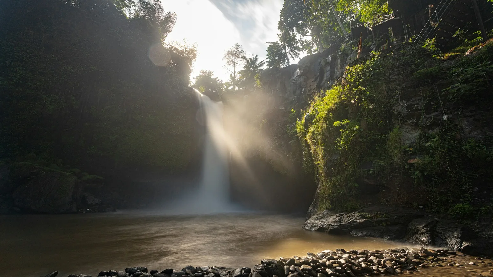 Morning sunbeams falling over Tegenungan Waterfall and its rocky pool near Ubud, Bali