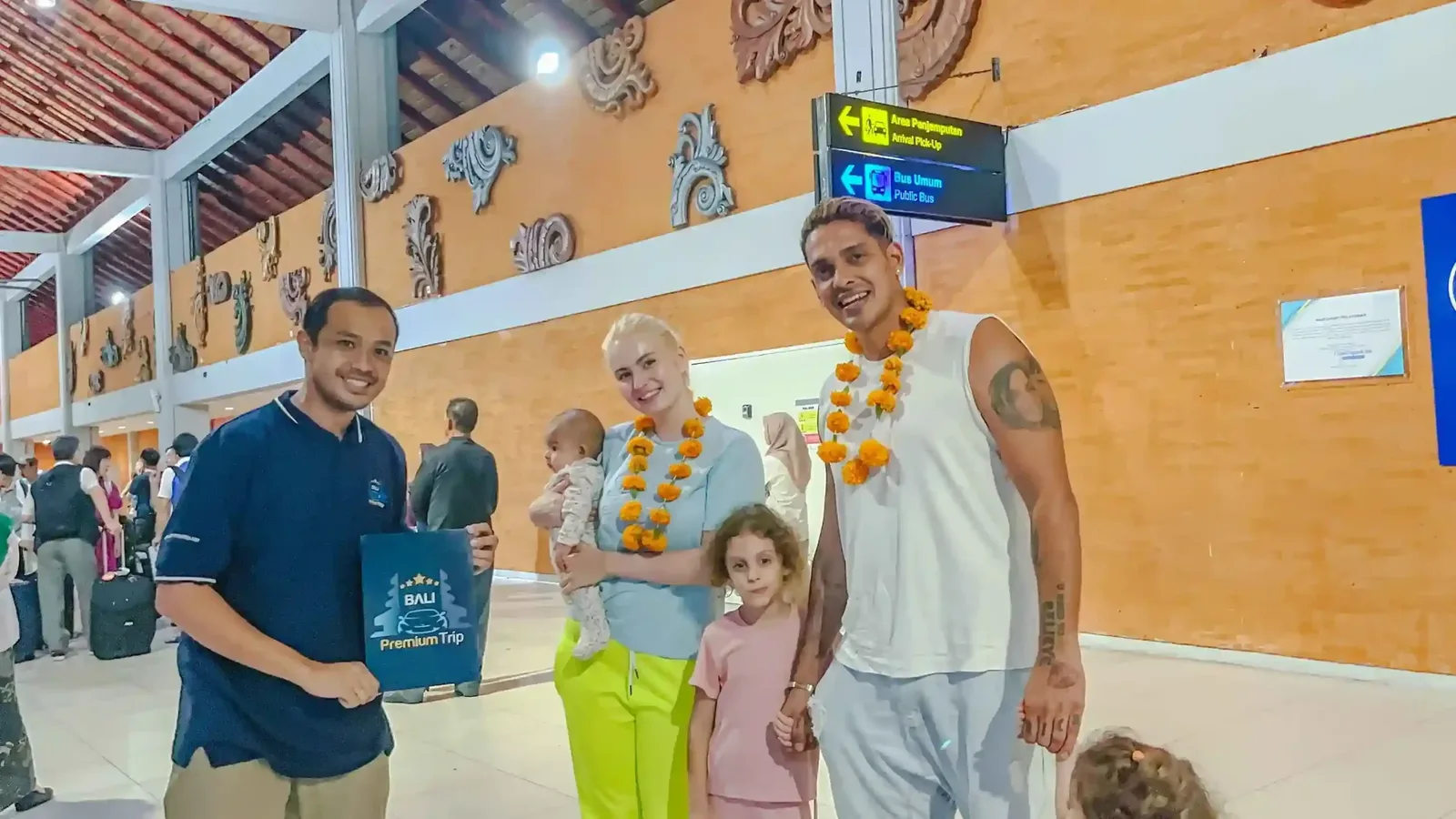 Greeter welcoming a family with flower garlands in the arrivals hall at Bali Ngurah Rai Airport