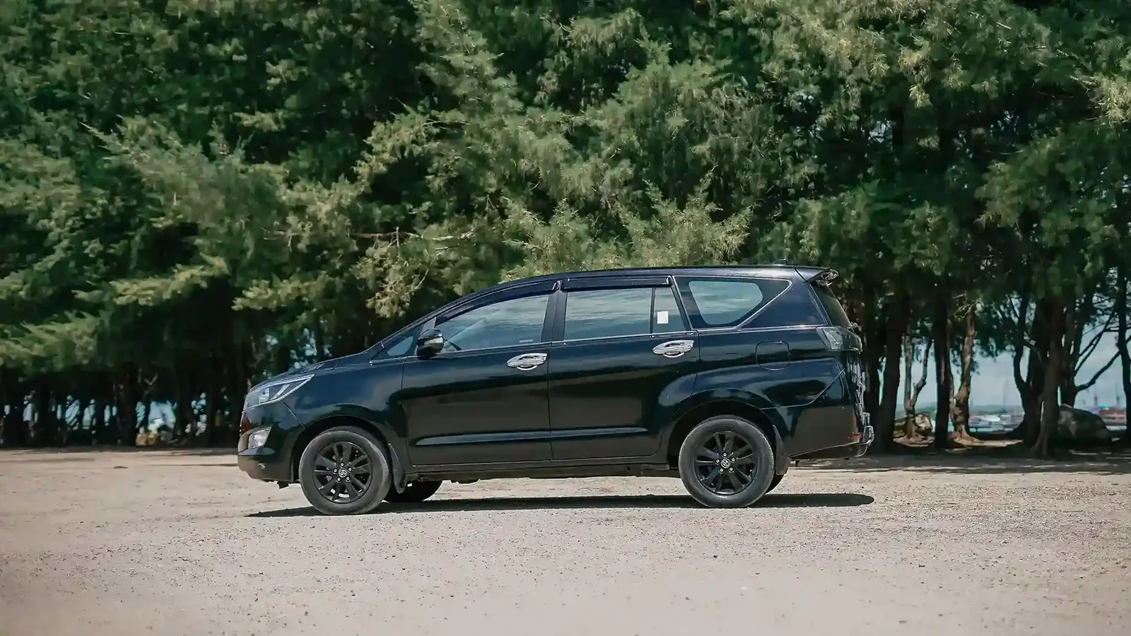 Black Toyota Innova private tour car parked under shady trees by the coast in Bali